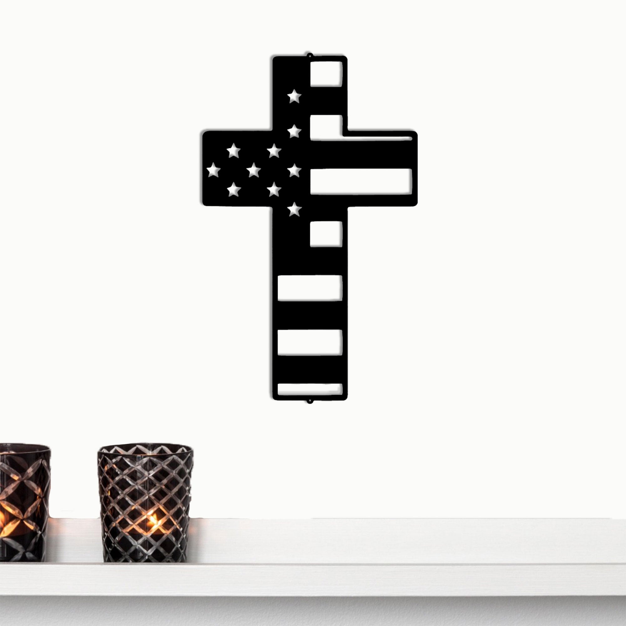 Black cross with American flag design on a white surface with two candles.
