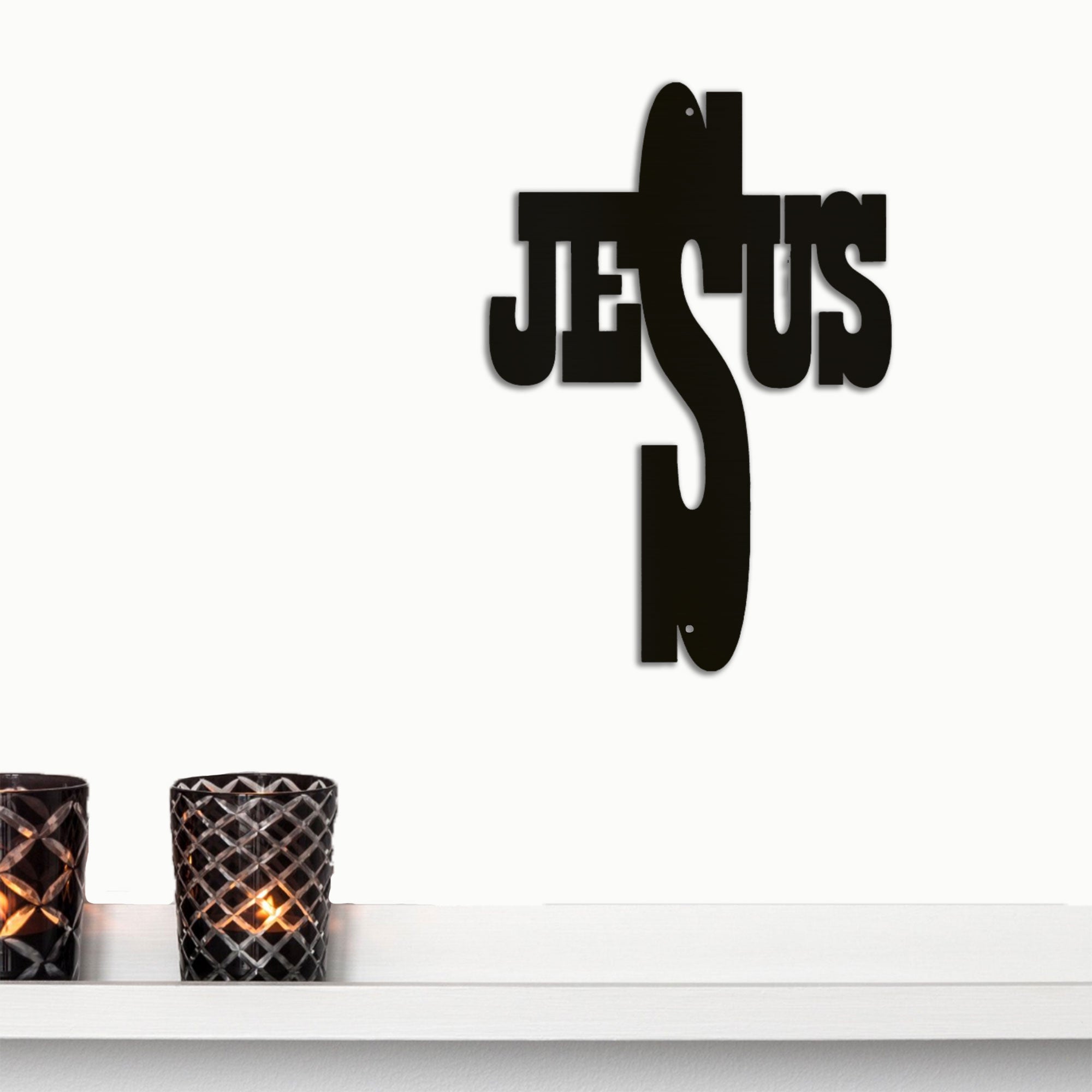 Black metal decorative piece spelling 'Jesus' on a white surface with candles.